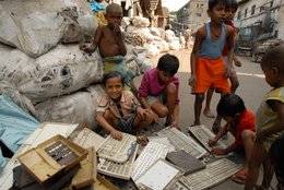 Kinder in Kalkutta auf Müllsäcken, vor ihnen Schulmaterial